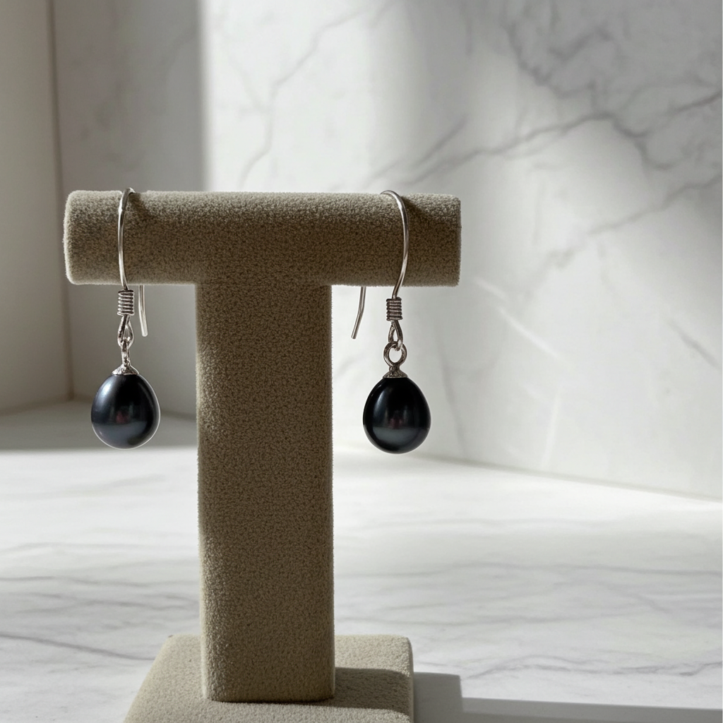 Boucle d'oreille pendante perle noire sur présentoir crème, fond marbré