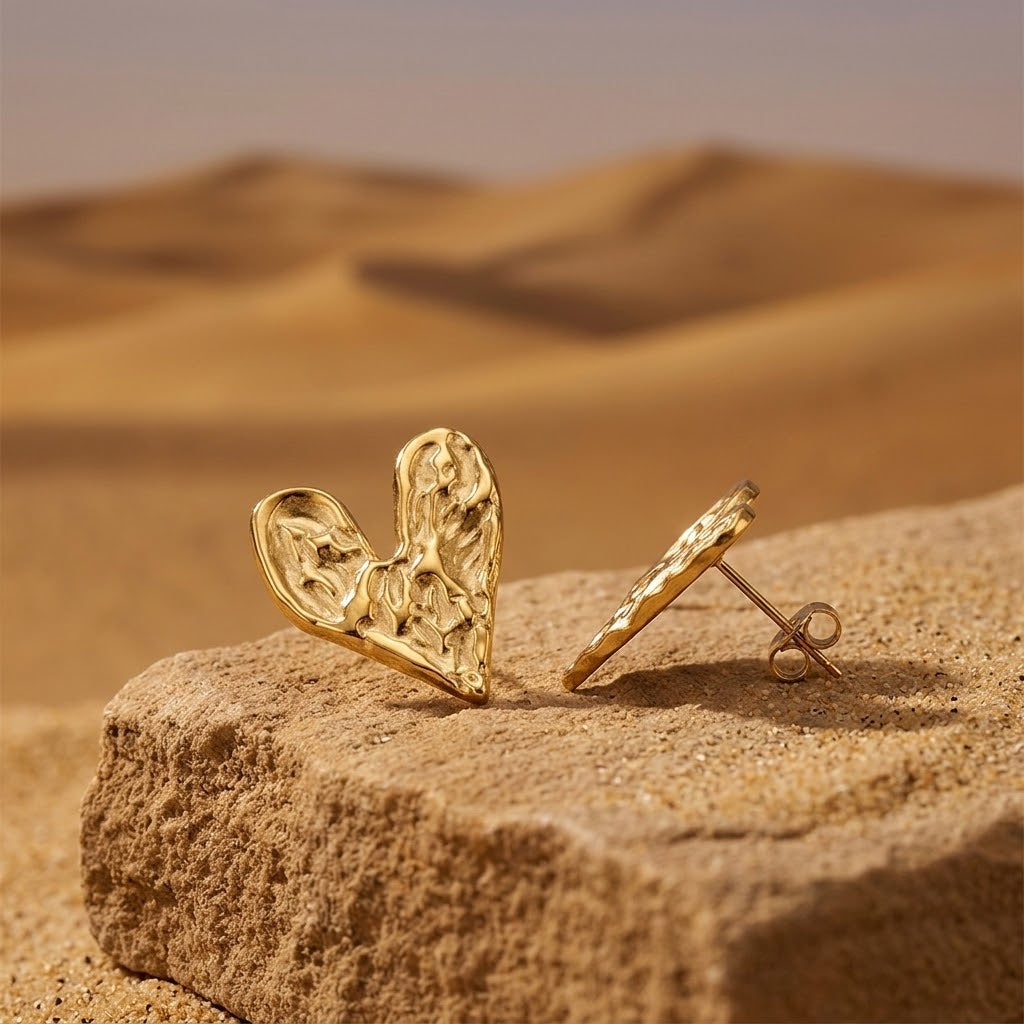 Boucles d'oreilles cœur martelé acier inoxydable 316L doré posées dans le sable ambiance désert lumière chaude - KENVIA 