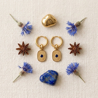 Boucles d’oreilles dorées et résine bleue présentées avec une sélection de fleurs et de matieres - KENVIA