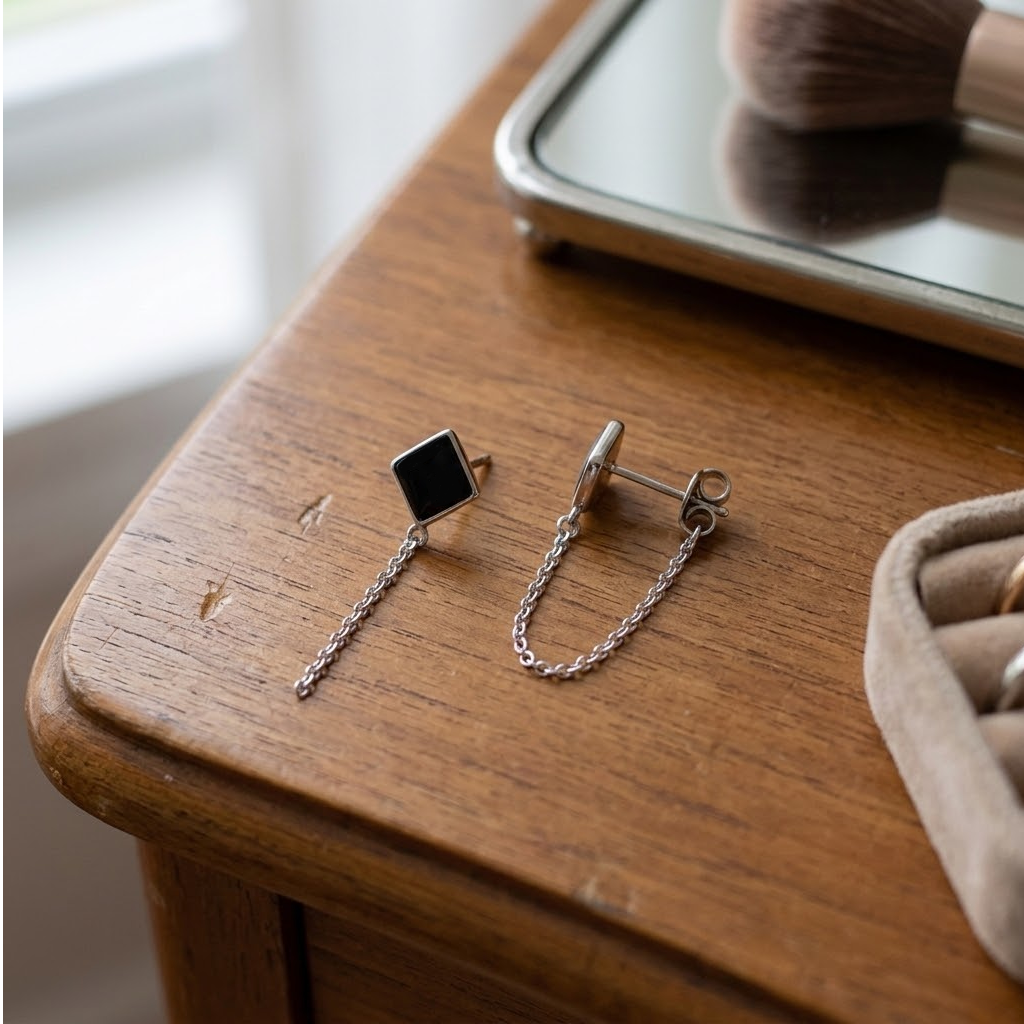 Boucles d’oreilles à losange noir et mini chaîne acier inoxydable 316L posées sur une table en bois, avec le fermoir poussette visible - KENVIA