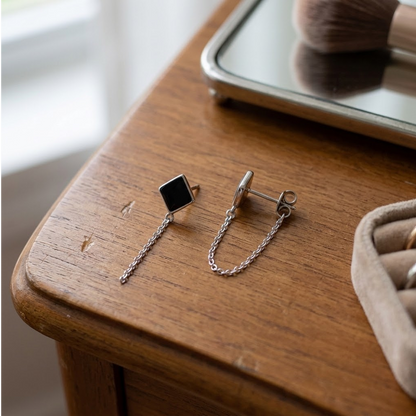 Boucles d’oreilles à losange noir et mini chaîne acier inoxydable 316L posées sur une table en bois, avec le fermoir poussette visible - KENVIA