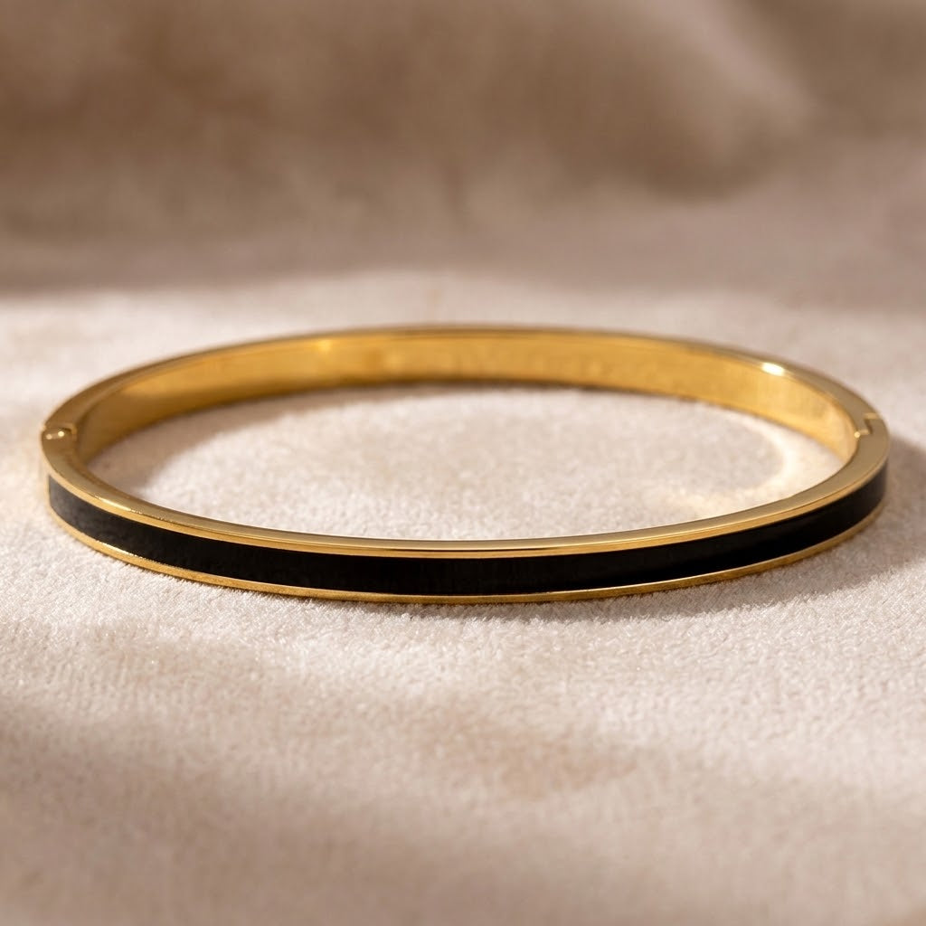 Bracelet jonc fin acier inoxydable 316L à finition dorée et émail noir posé sur une surface claire - KENVIA