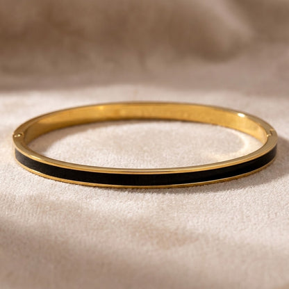 Bracelet jonc fin acier inoxydable 316L à finition dorée et émail noir posé sur une surface claire - KENVIA