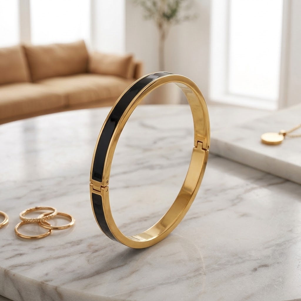Bracelet jonc fin en acier inoxydable 316L à finition dorée avec incrustation noire et fermoir à charnière, posé sur une table en marbre blanc