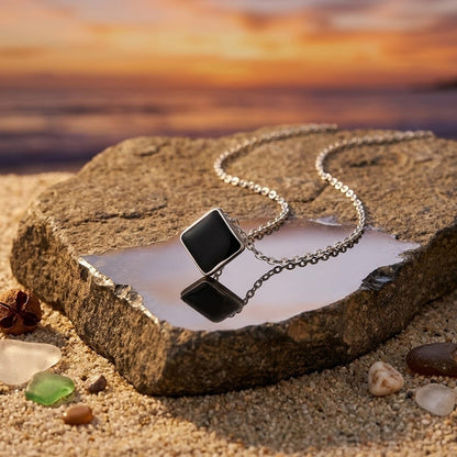 Collier à pendentif losange noir présenté dans une composition avec un paysage au coucher du soleil en arrière-plan -KENVIA