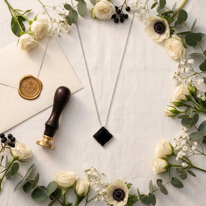 Collier à pendentif losange noir présenté à plat dans une composition florale - KENVIA
