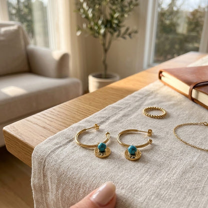Demi-créoles dorées avec détail turquoise présentées sur une table de séjour - KENVIA